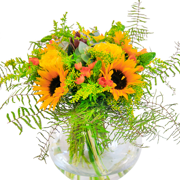 This sun-drenched bouquet is a tribute to the peak of summer in Great Bookham, brimming with vitality and emotional resonance. Vibrant sunflowers stand tall and proud, their bright yellow petals fanning out around dramatic dark centres-each bloom like a beacon of light against the background of the local High Street. In close harmony, golden yellow roses bloom with intricate whorls, highlighting the florist's meticulous technique and love for classic garden varieties. Cheerful clusters of glossy red Hypericum berries dot the scene, sparkling amidst a generous layering of verdant foliage. Wisps of fern cascade over the edge, imbuing the design with softness and movement, while fine sprigs of light green solidago-adorned with miniature yellow blossoms-add delicate highlights throughout. Soft blue-green eucalyptus leaves peek playfully from within, enhancing the natural and slightly rustic feel. All stems are securely nestled into a round, transparent glass vase, where the interplay of submerged greens and the shimmering surface of clear water evoke Great Bookham's peaceful ponds and clear skies. The arrangement balances a refined sense of abundance and spontaneity, easily imagined as the heart of a lively family gathering or a thoughtful gift marking a joyful occasion. Created by local experts passionate about their craft, this bouquet stands as a perfect gesture for birthdays, anniversaries, or simply to bring a touch of sunlit exuberance into any Great Bookham home.